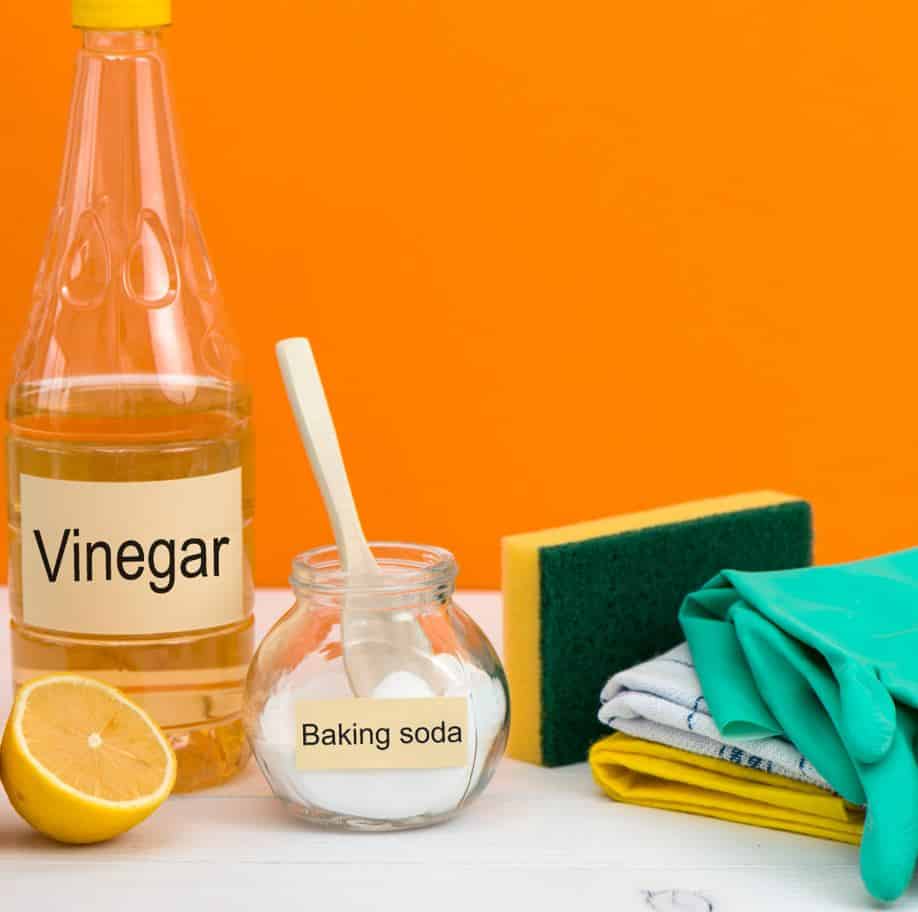 a bottle of vinegar, jar of baking soda, lemon and other assorted cleaning products on a white table
