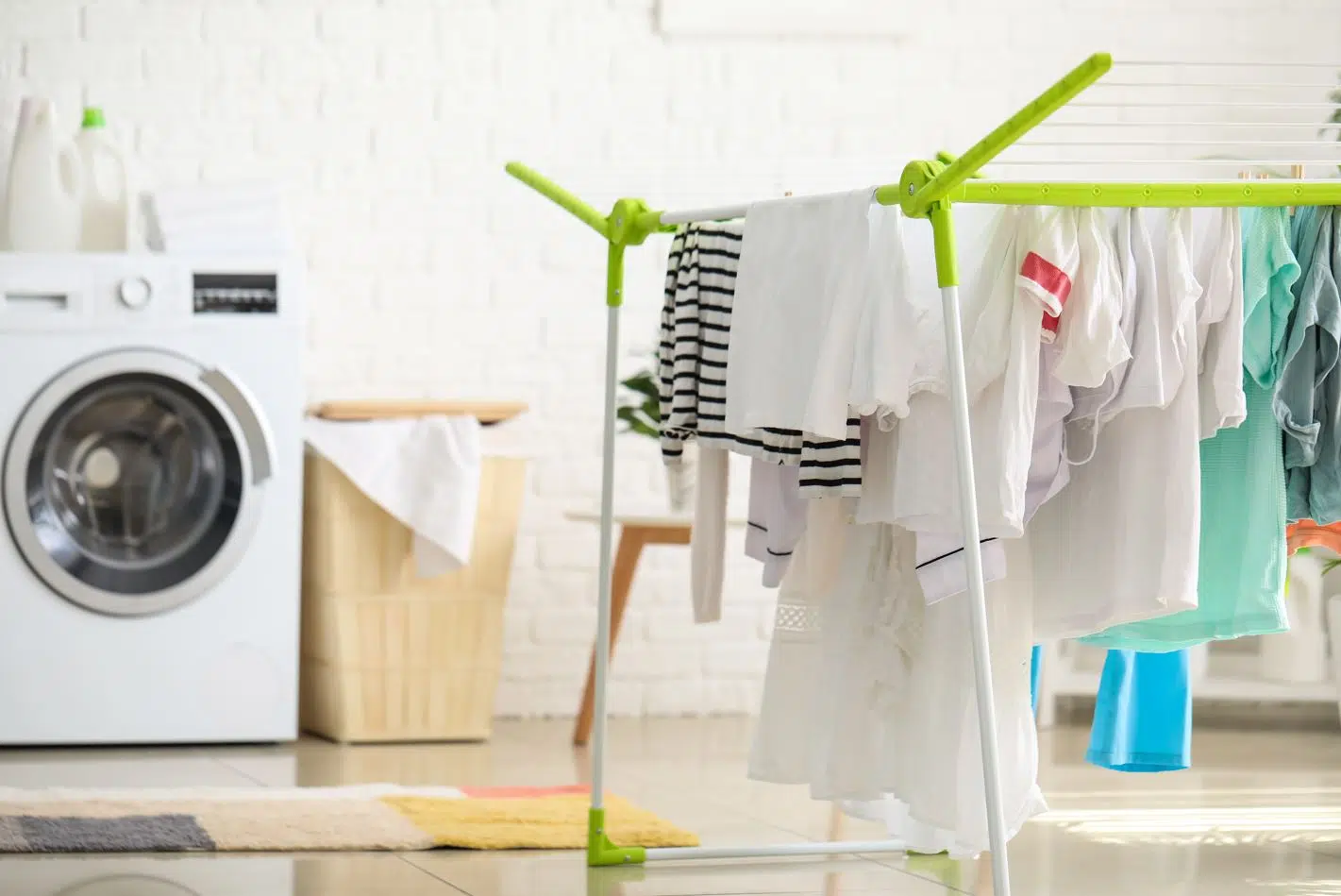 clothes hanging on a portable clothesline in the foreground with a dryaer and clothes basket in the background