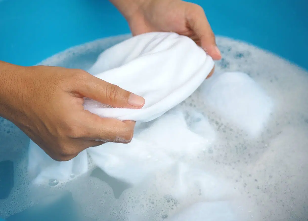 man treating white stained shirt in a blue bucket of soapy water