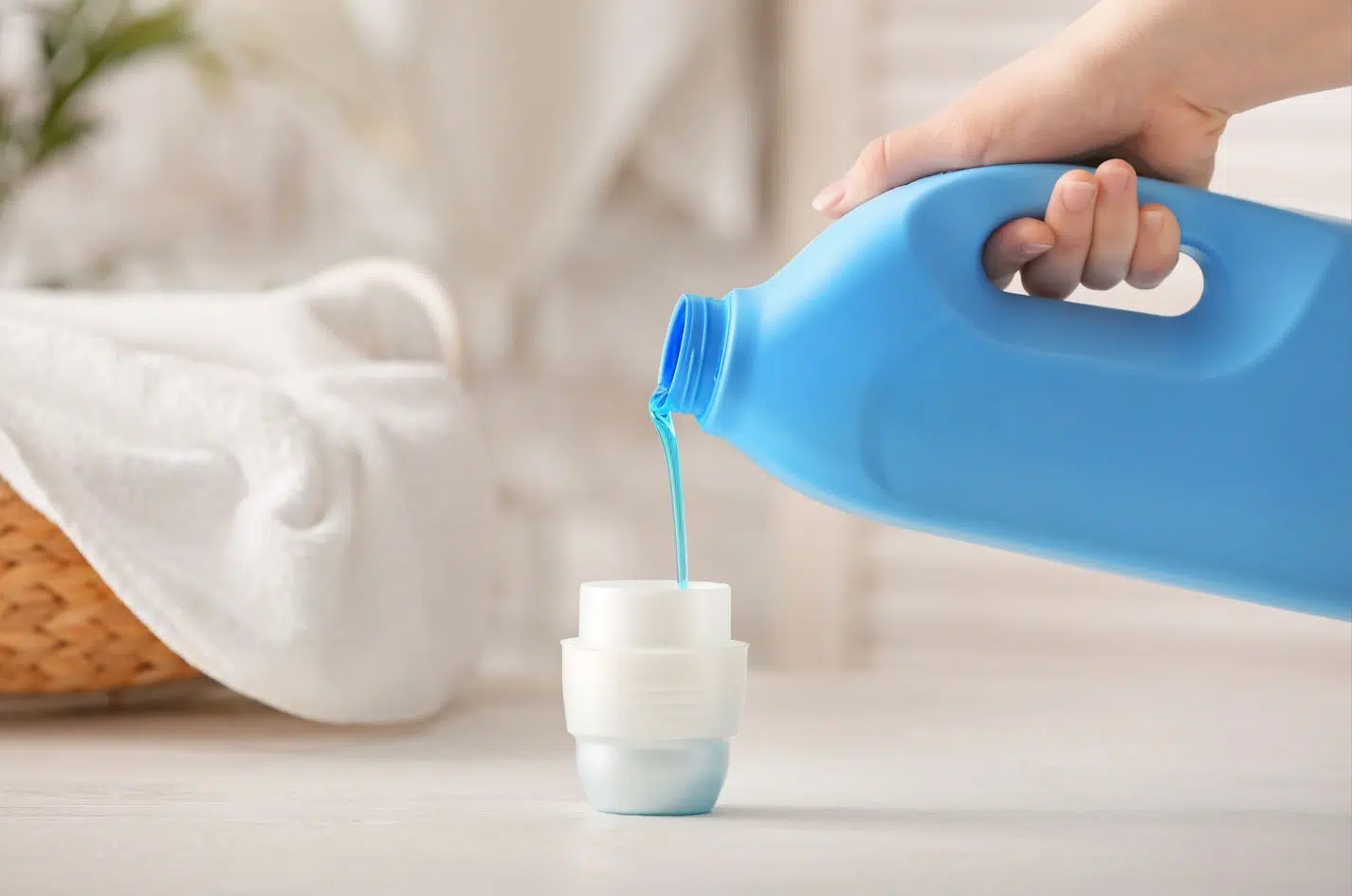 woman pouring blue laundry liquid into a cup lid