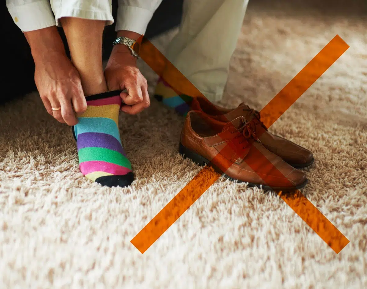 man putting woolen socks on next to brown lofers with an orange cross mark