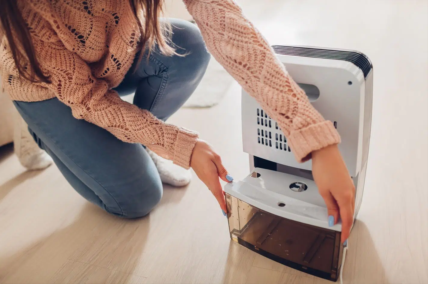 woman with blue nail polish opening water chamber on white dehumidifier