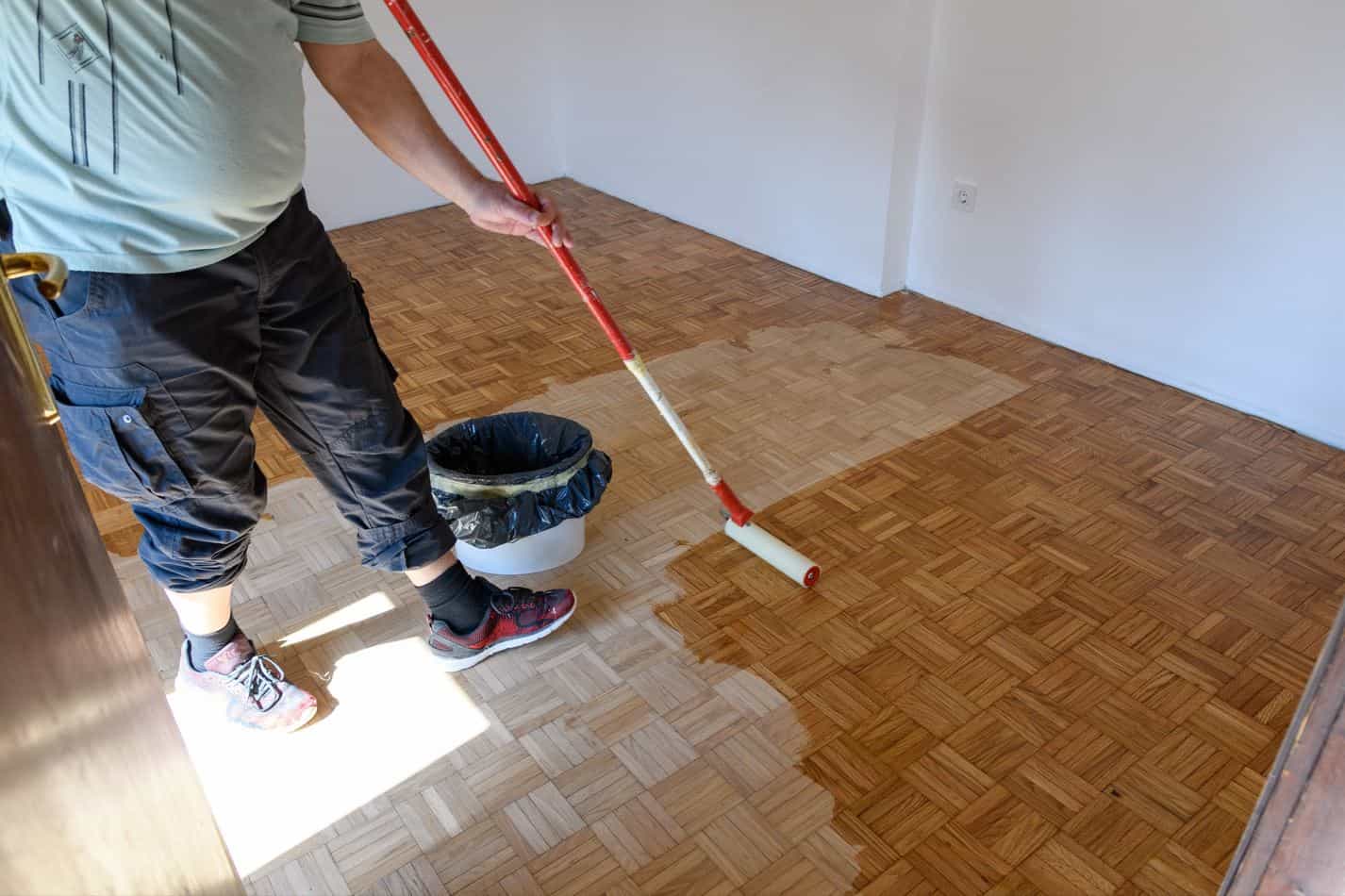 man applying laquer to hard oakwood floor with a red rolling brush