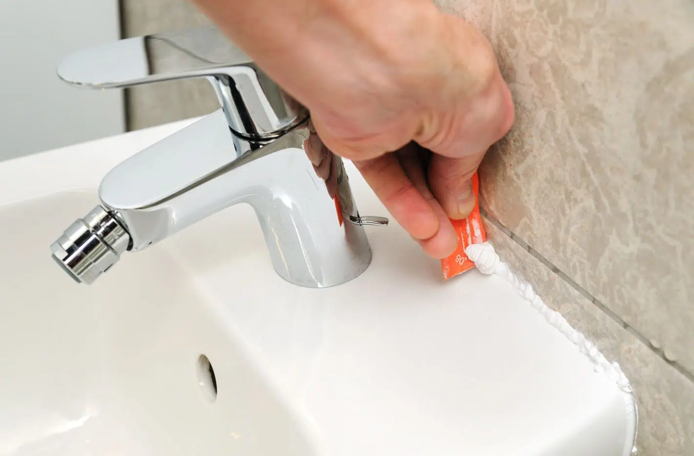 man using tool to remove caulk from bathroom vanity