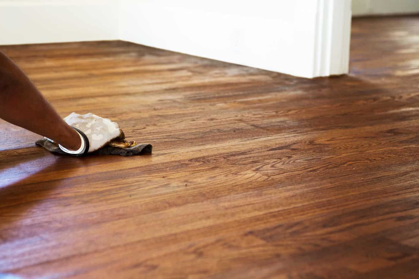 man wearing white rubber gloves using a cloth to relaquer hardwood flooring