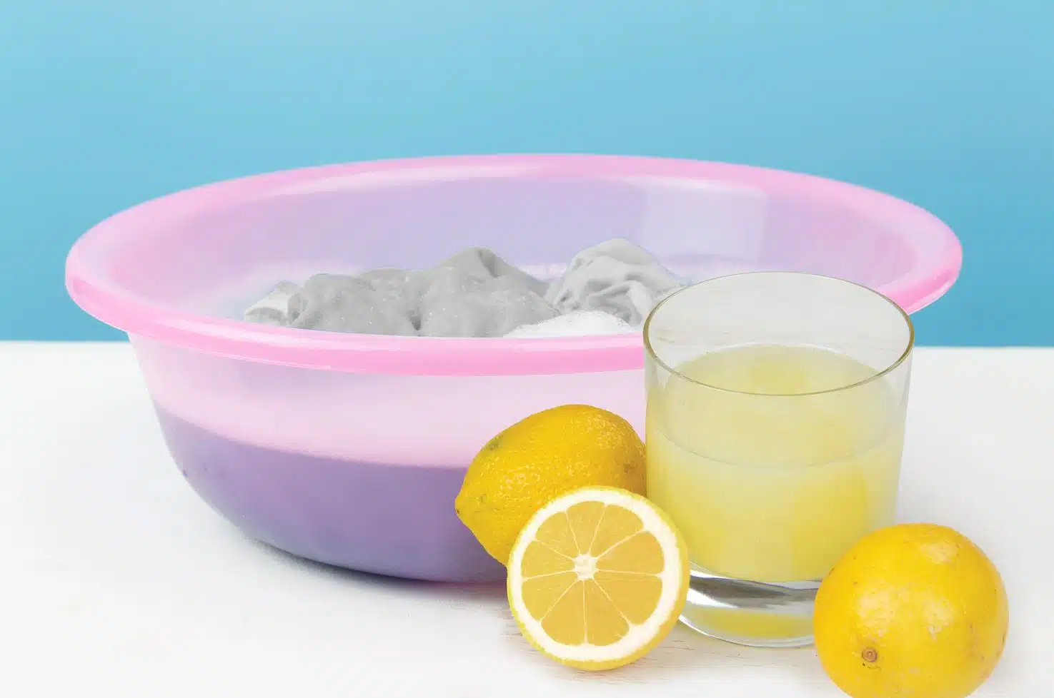 glass of lemon juice next to a pink bowl of white clothes soaking