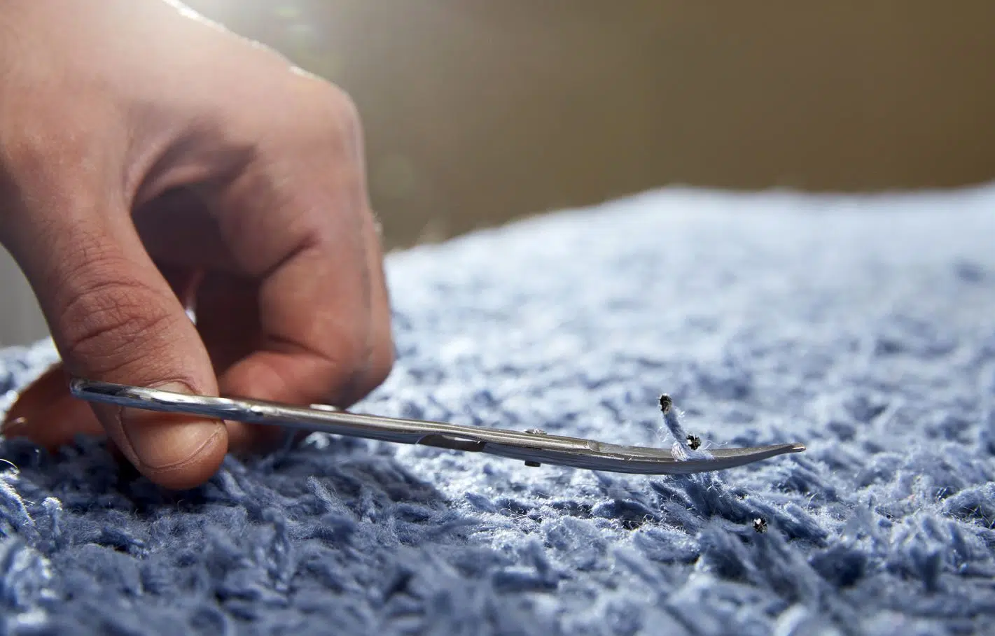 man using scissors to fix carpet burn on blue carpet