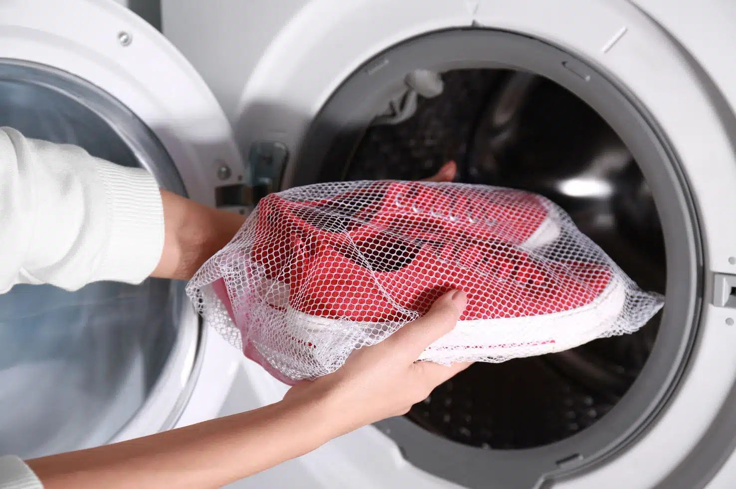 woman putting red converse all stars in a wash safe mesh bag into front loader washing machine