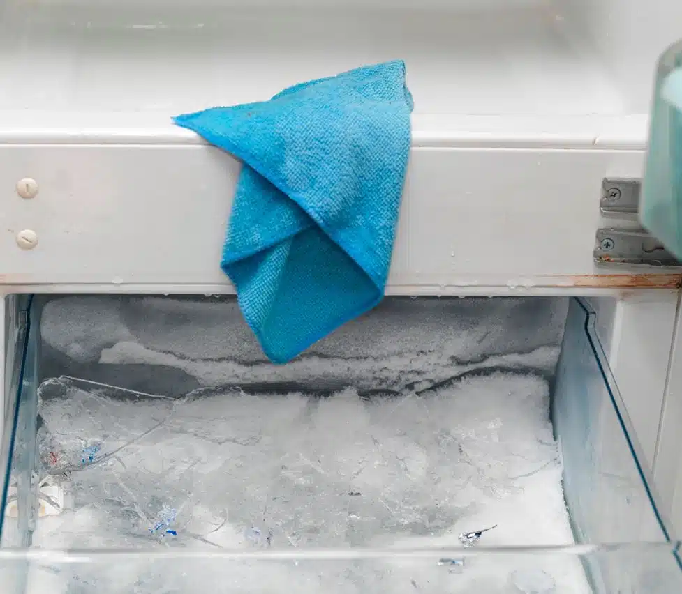 blue microfibre cloth sitting in an empty fridge after being used to clean freezer