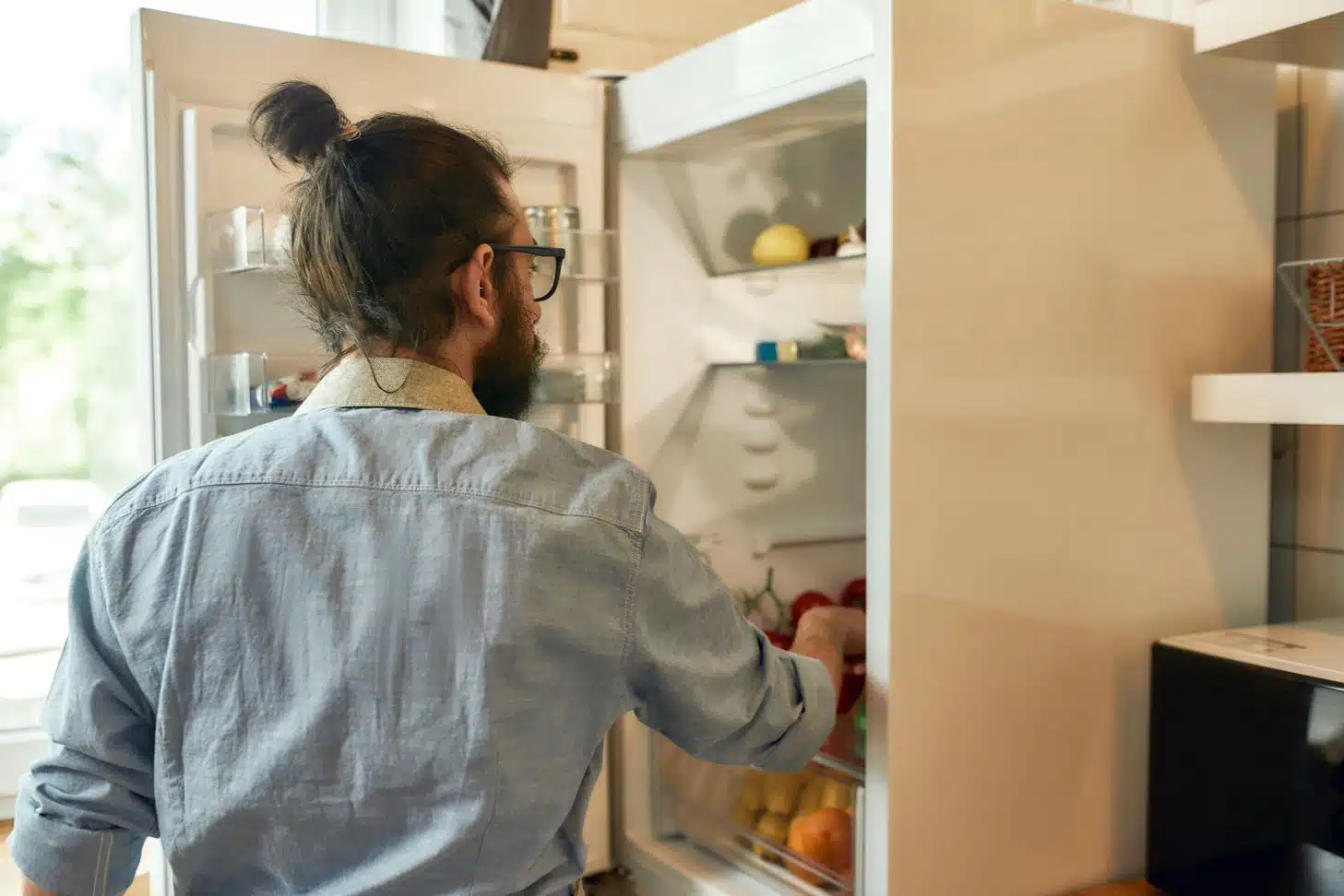 close up of man with pony tail looking into a full organised single door fridge