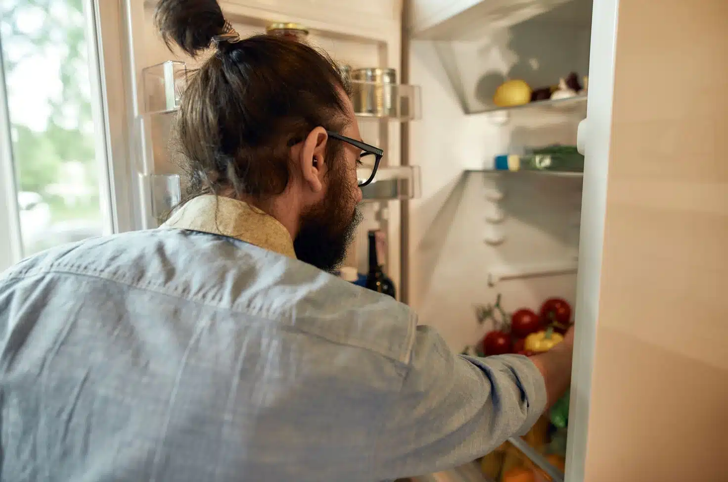 close up of man with pony tail organising a large open fridge