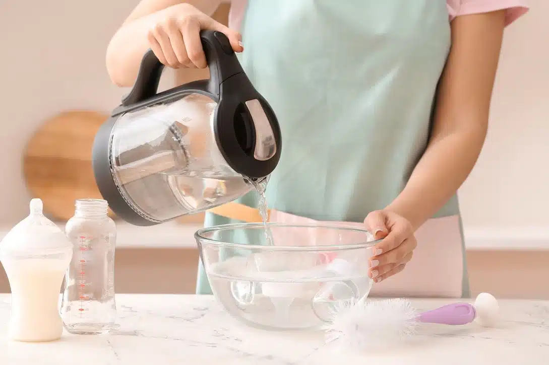 woman disinfecting babies bottles in a large pyrex bowl of hot water
