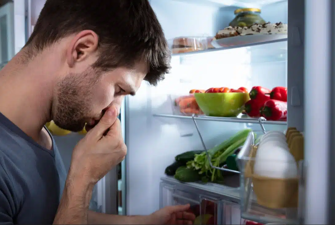 man in open fridge holding nose