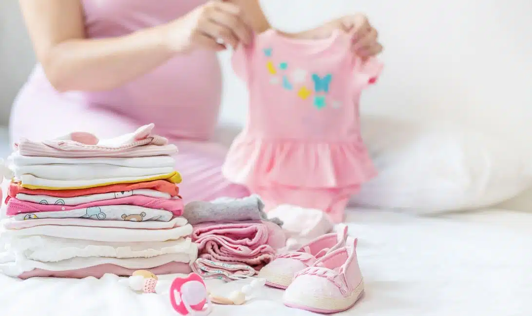 pregnant woman wearing pink t-shirt folding pink onesie