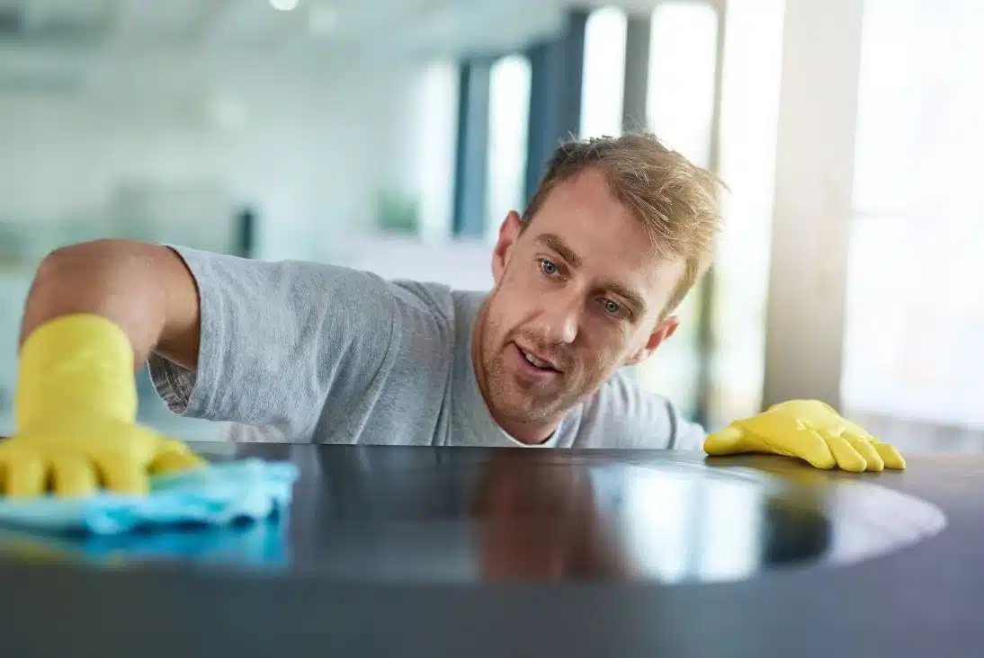 blonde haired man with yellow gloves cleaning the top of a kitchen cabinet