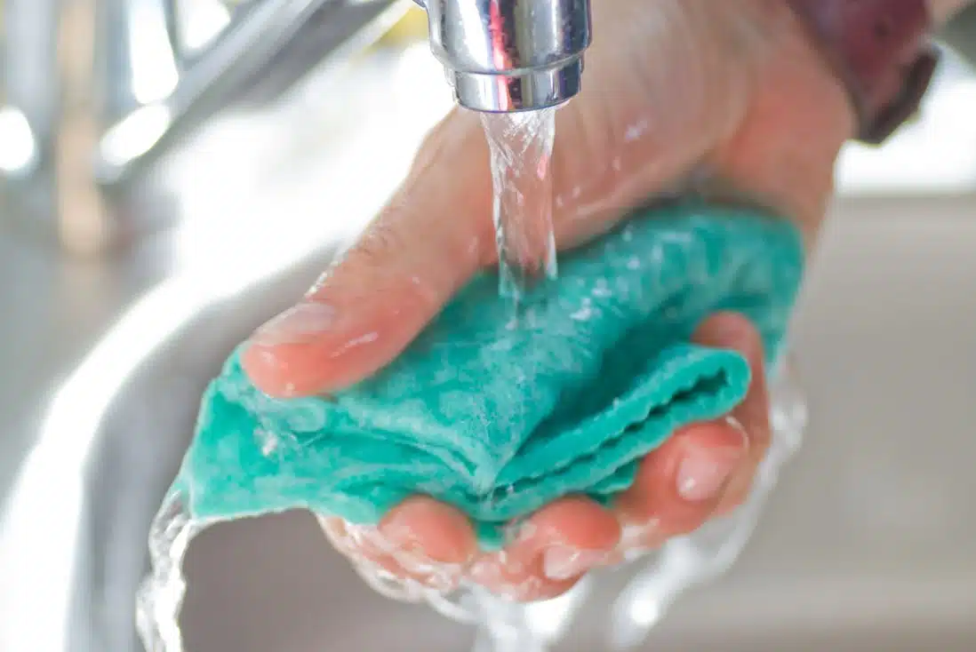 blue microfibre cloth being rinsed under a tap