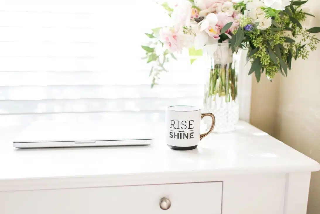 clean white tabletop with macbook and clear vase of flowers in the background