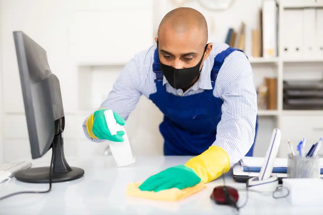 man cleaning computer desk station with black mask on