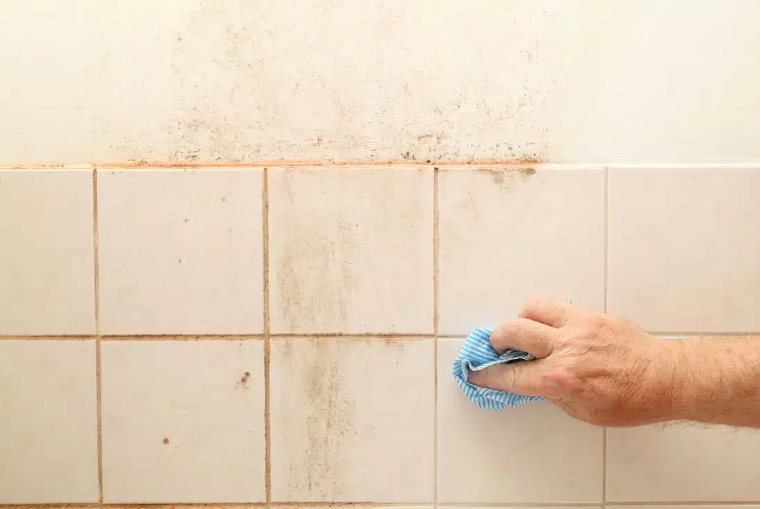 man cleaning pink mould on the tiles of a dirty bathroom
