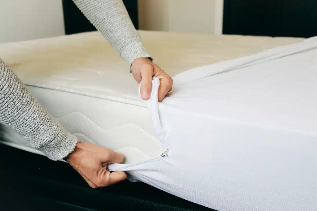 man pulling white mattress protector over dirty white mattress