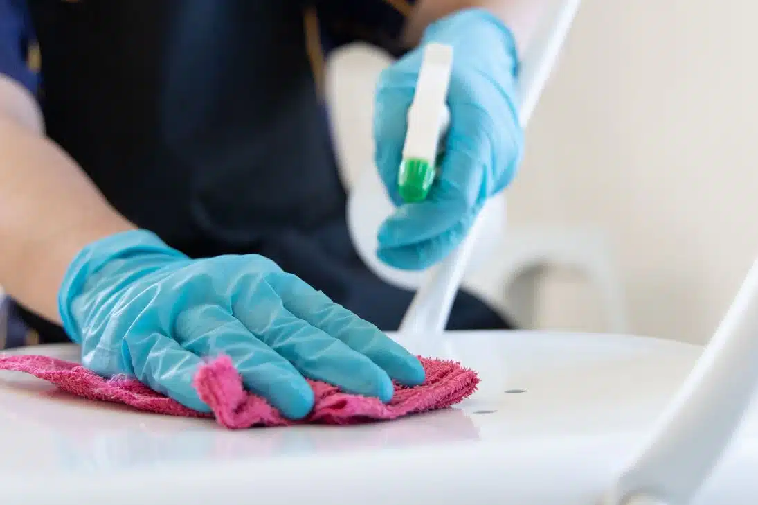 woman wearing blue gloves using a pink microfibre cloth to wipe down white plastic chair