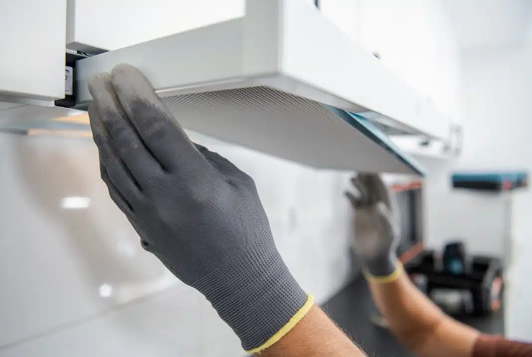 person wearing black gloves putting rangehood filter back in place