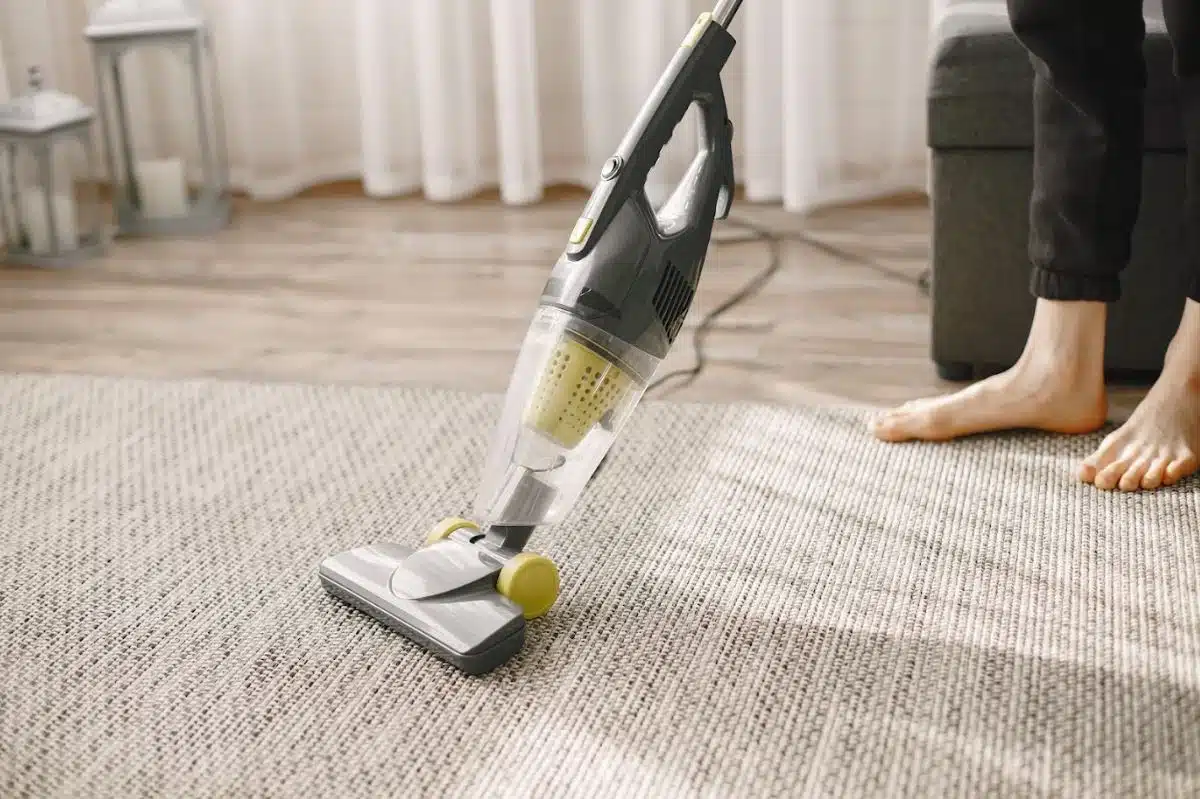 man using handheld vacuum on a beige throw down rug