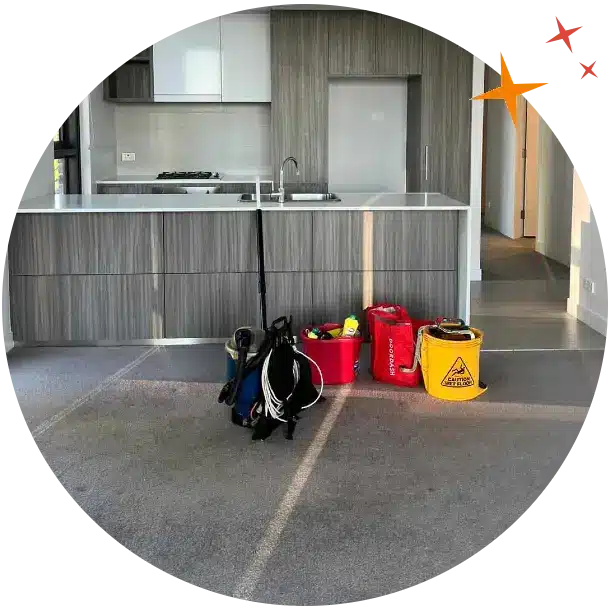 Empty apartment kitchen with backpack vacuum, yellow mop bucket and red cleaning caddy in the foreground.